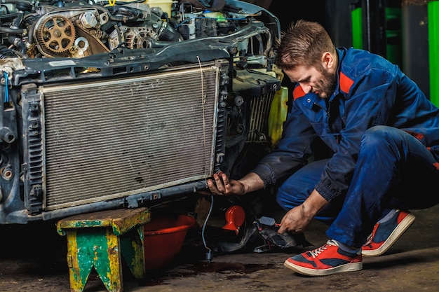 Un mecánico cansado con un traje protector azul está reparando el radiador de un automóvil.