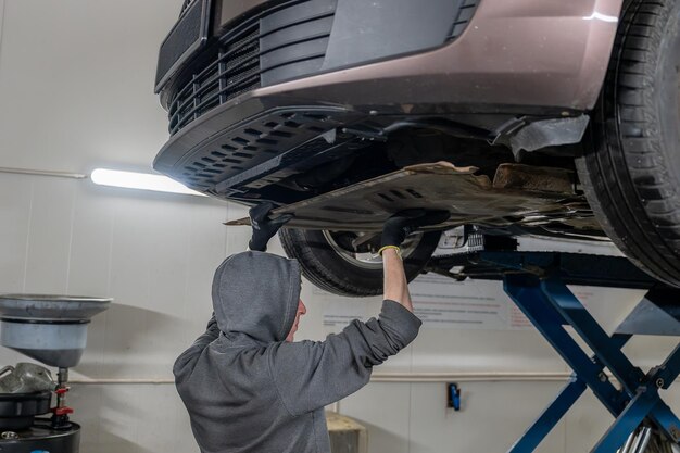 Mecánico con capucha y guantes trabajando en el tren de aterrizaje de un automóvil en un taller de reparación