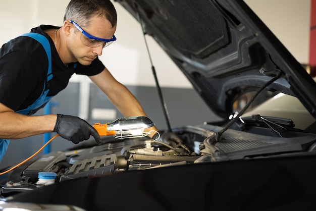 Mecánico caucásico con overoles azules está trabajando en un automóvil en un reparador de servicio de automóviles con gafas de seguridad