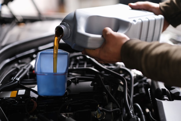 Mecánico de cerrajería vierte aceite de motor en un recipiente de plástico en el motor del motor