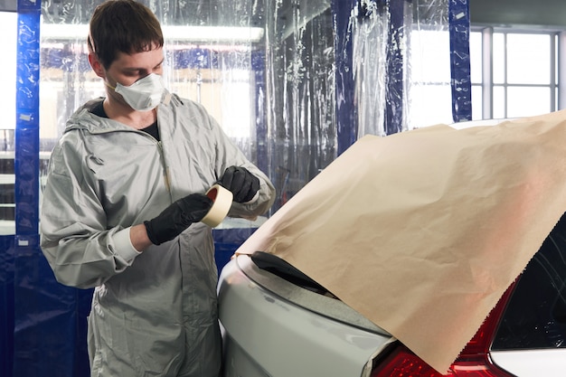 Foto mecânico, cobrindo o carro com papel antes de pintar no serviço de reparo de automóvel