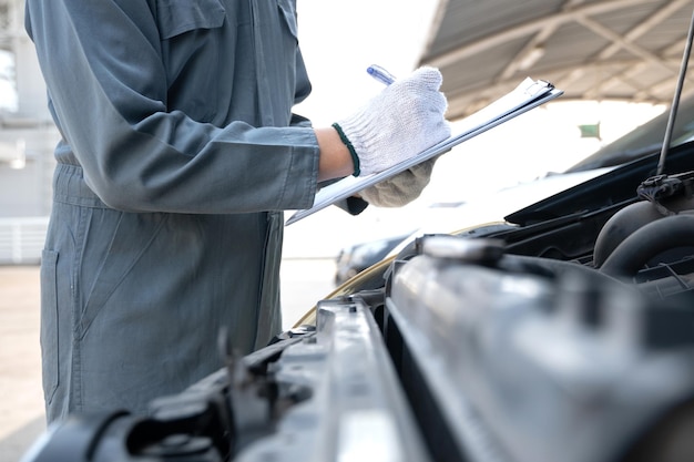 Mecánico comprobando el motor de un automóvil y tomando notas
