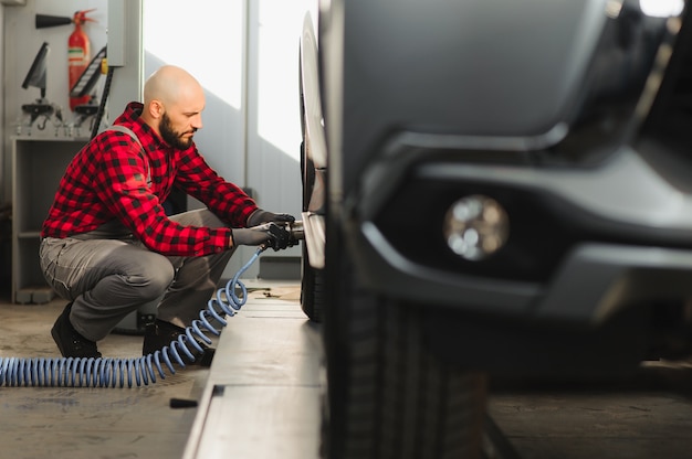 Mecânico de automóveis aparafusando roda de automóvel levantado