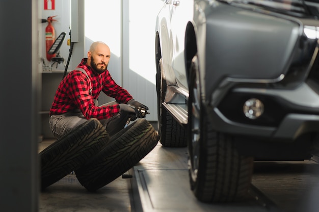 Mecânico de automóveis aparafusando roda de automóvel levantado