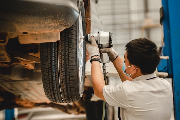 Mecânico de automóveis asiático está trocando um pneu novo em uma oficina de troca de pneus