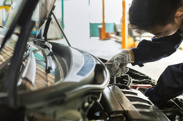 Mecânico de automóveis asiático homem usando uma chave para atender o carro na garagem.