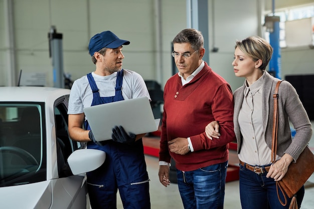 Mecânico de automóveis conversando com um casal enquanto estiver usando laptop na oficina mecânica