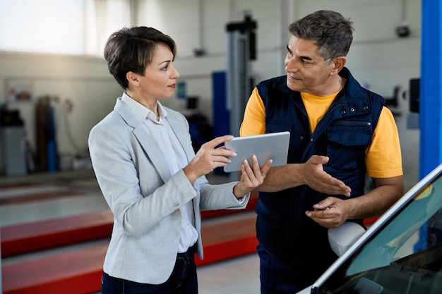 Mecânico de automóveis e gerente feminino cooperando ao usar o touchpad na oficina de automóveis