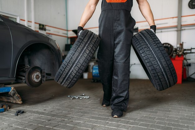 Mecânico de automóveis mantém dois pneus novos, serviço de conserto. trabalhador conserta pneu de carro na garagem, inspeção profissional de automóvel na oficina