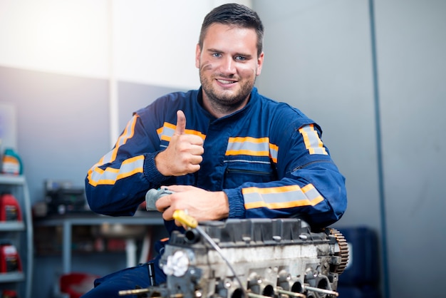 Mecânico de automóveis parado junto ao motor do carro com os polegares para cima.