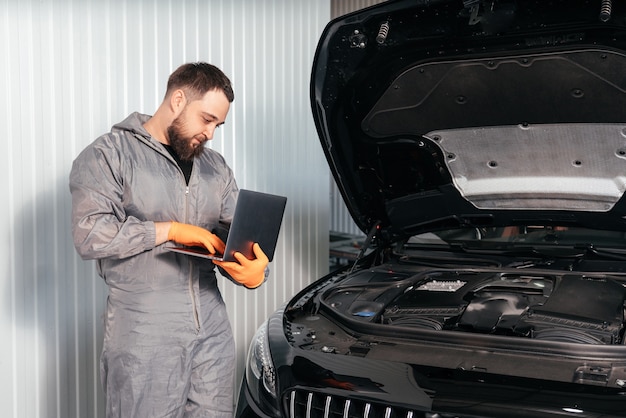 Mecânico de automóveis trabalhando com um laptop em serviço de conserto de automóveis, verificando o motor do carro