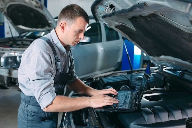 Mecânico de automóveis usando um laptop para diagnosticar e verificar as peças do motor do carro para conserto e reparo