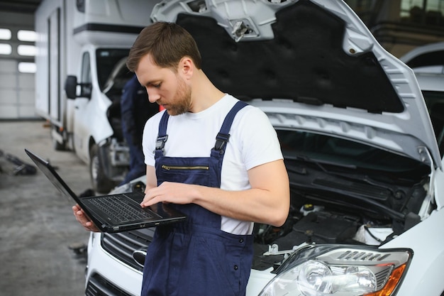 Mecânico de automóveis usando um laptop para diagnosticar e verificar as peças do motor do carro para conserto e reparo