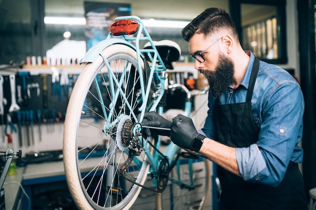 Foto mecânico de bicicleta jovem barba consertando bicicletas em uma oficina.