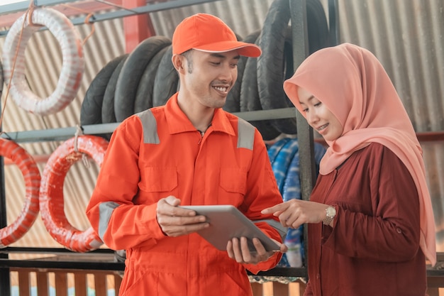 Mecânico em um uniforme do wearpack e uma cliente usando um tablet digital para visualizar o catálogo em uma oficina de peças sobressalentes