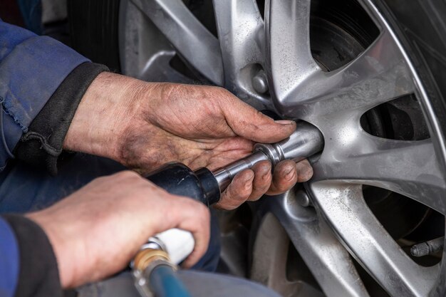 El mecánico está cambiando la rueda del automóvil con una llave neumática