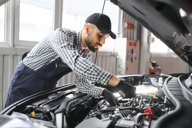 Mecánico examinando bajo el capó del coche en el garaje de reparación