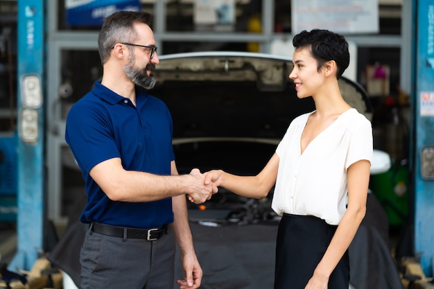 Mecánico experto estrechar la mano del cliente satisfecho y trabajar en el garaje de la estación de mantenimiento de reparación de automóviles. Satisfacción en el servicio.