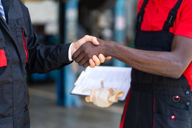 Mecánico experto estrechar la mano del cliente satisfecho y trabajar en el garaje de la estación de mantenimiento de reparación de automóviles