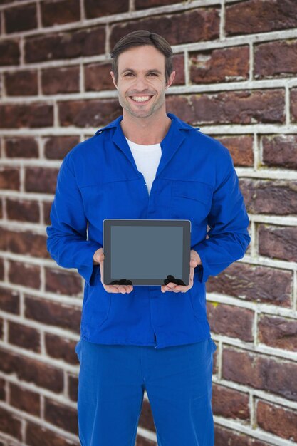 Mecânico feliz segurando tablet digital contra a parede de tijolos vermelhos