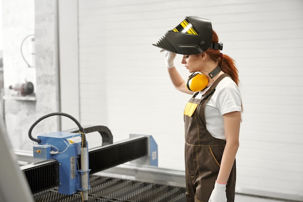 Foto mecánico femenino en máscara protectora de pie cerca de cnc