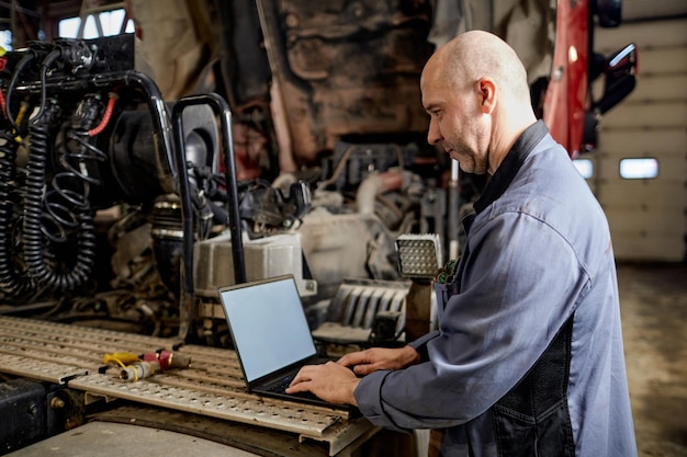 Mecánico inspeccionando el motor usando una computadora portátil en un taller de garaje
