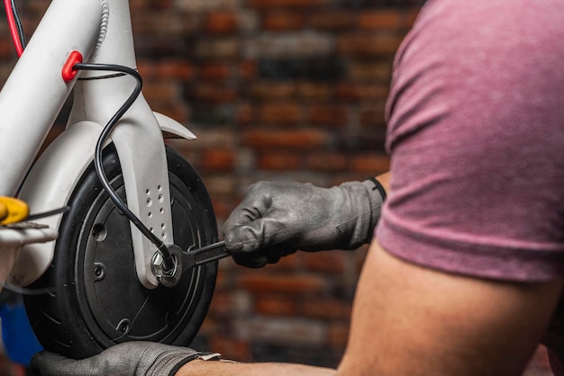 Un mecánico irreconocible sosteniendo y ajustando la rueda del scooter eléctrico con una llave en su taller.