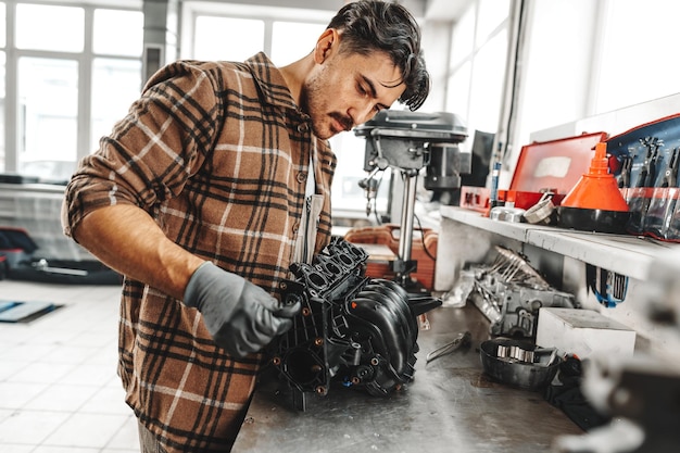 Mecânico jovem reparando peças de carros na mesa de trabalho na oficina de automóveis