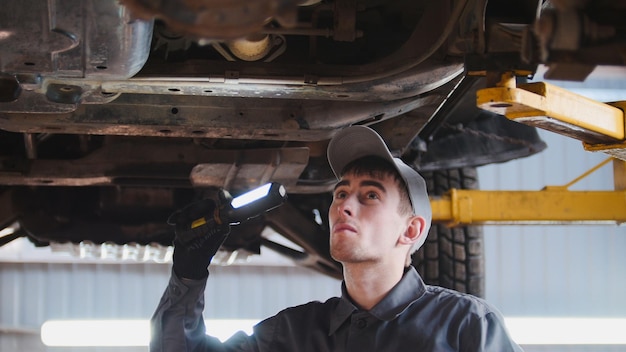 Mecánico con lámpara thr está comprobando la parte inferior del coche en el garaje de servicio de automóviles