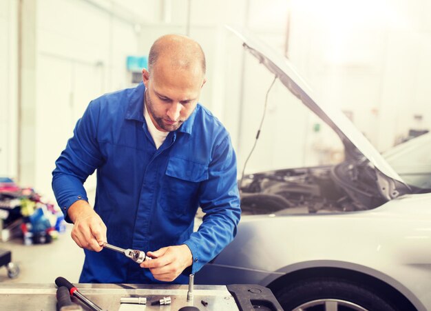 Foto mecánico con llave inglesa reparando un coche en el taller