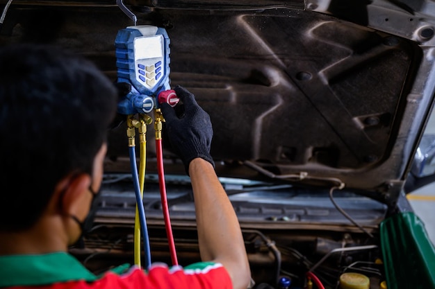 El mecánico masculino asiático llena el refrigerante del automóvil y verifica que el sistema de aceite del compresor del aire acondicionado del automóvil que excede el aire acondicionado del automóvil no esté frío