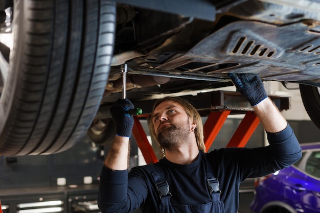 Un mecánico masculino con una llave desenrosca las tuercas en la parte inferior del automóvil que está en el ascensor Mantenimiento profesional de automóviles en el servicio