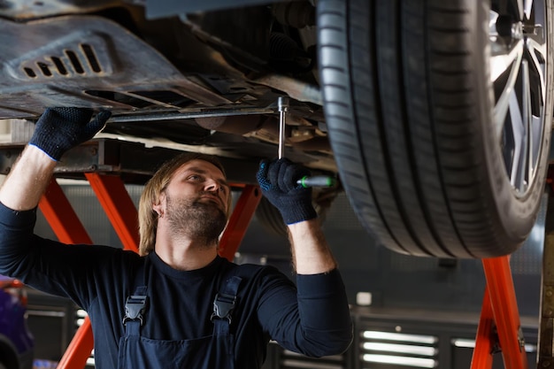 Un mecánico masculino con una llave desenrosca las tuercas en la parte inferior del automóvil que está en el ascensor Mantenimiento profesional de automóviles en el servicio