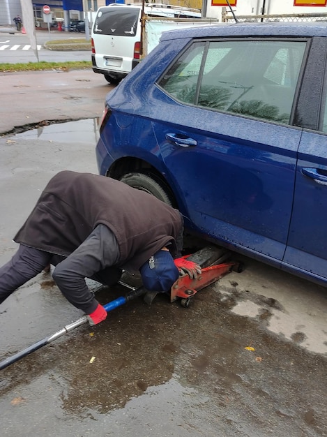 El mecánico mira debajo del auto para levantarlo con un gato y reemplazar la rueda