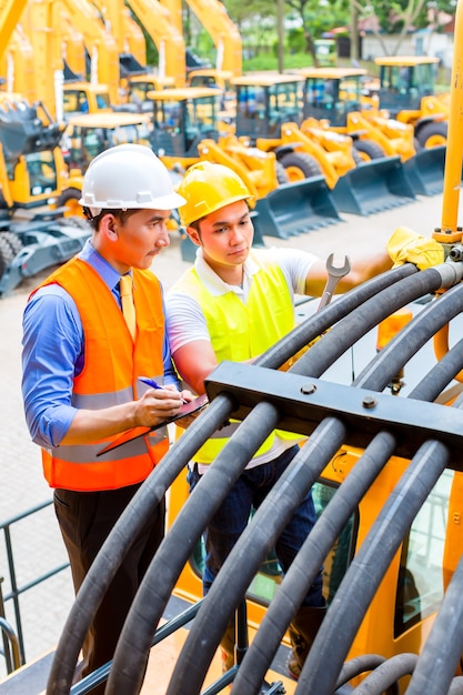 Mecânico motorizado asiático discutindo com a lista de tarefas do engenheiro na oficina de máquinas de construção