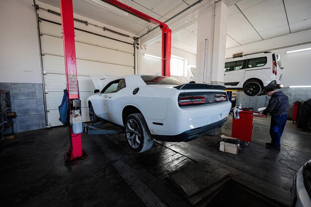 Mecânico na estação de reparação de serviço trabalhando com muscle car no elevador