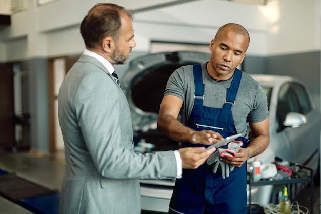 Foto mecánico negro y hombre de negocios usando tableta digital en el taller de reparación de automóviles