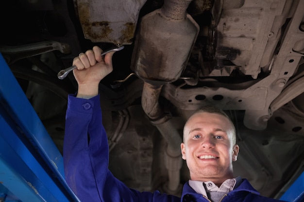 Mecânico olhando câmera abaixo de um carro