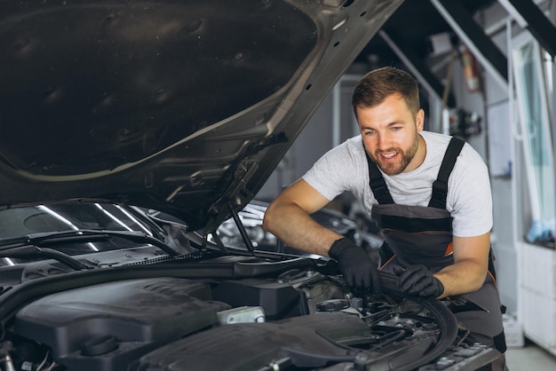 Mecánico profesional sonriendo mientras trabaja en un motor de automóvil en un taller de reparación de automóviles