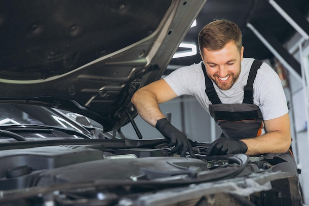 Mecánico profesional sonriendo mientras trabaja en un motor de automóvil en un taller de reparación de automóviles