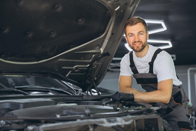 Mecânico profissional sorrindo enquanto trabalha em um motor de carro em uma oficina de reparação de automóveis