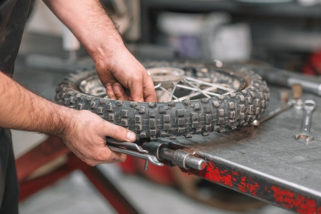 Mecánico que repara el neumático dañado de la motocicleta, en taller de reparaciones.