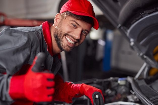 Foto mecánico reparando auto y mostrando el pulgar hacia arriba