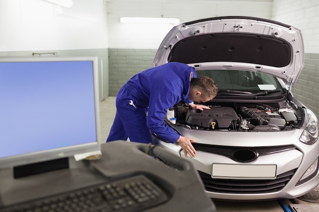 Mecánico reparando un automóvil al lado de una computadora