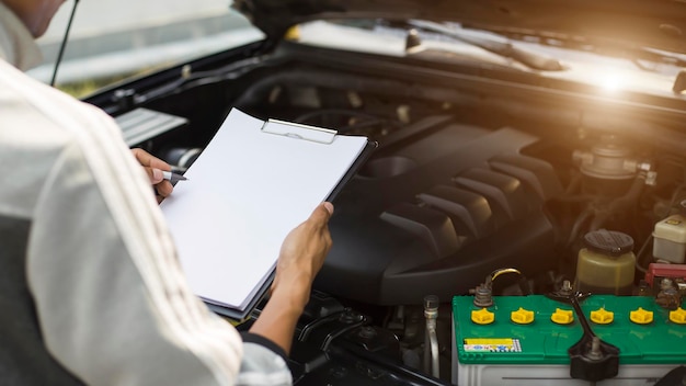 El mecánico revisa el motor de los autos y lo guarda en el clip de la lista de verificación de servicio de reparación y mantenimiento