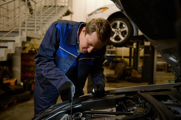 Mecánico revisando y reparando el motor del automóvil, técnico inspeccionando el motor de un automóvil con el capó abierto en el taller de reparación. Mantenimiento de automóviles, consumismo, personas y concepto laboral.