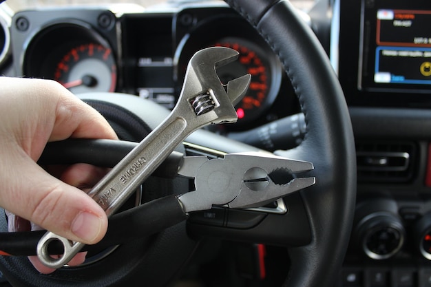 Mecânico segura ferramentas de reparo na frente do volante e conjunto de instrumentos desfocado no carro