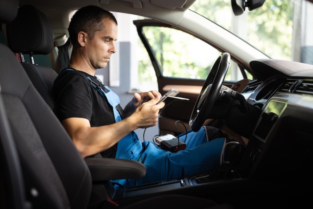 Mecânico sentado no carro e trabalhando no laptop enquanto faz o teste de diagnóstico do veículo no serviço automático