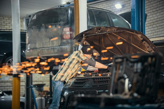 Foto mecánico de servicio de reparación de automóviles parado junto al automóvil con el capó abierto y haciendo su trabajo chispas de fuego