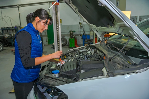 Mecánico de sexo femenino joven que comprueba el filtro de aire de un motor de coche